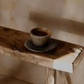 Ceramic cup and saucer on a rustic wooden stool against a beige wall.