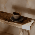 Ceramic cup and saucer on a rustic wooden stool against a beige wall.