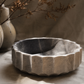 Decorative stone bowl on a neutral background with a vase and branches.