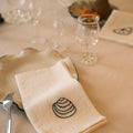 Linen napkin with shell design on a table setting with cutlery and glasses.