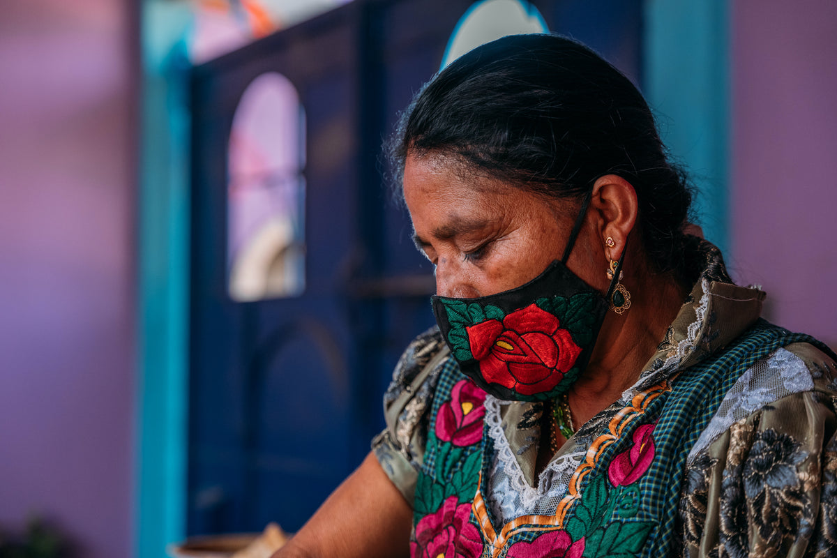 Macrina wears a rose embroidered mask while working on something.
