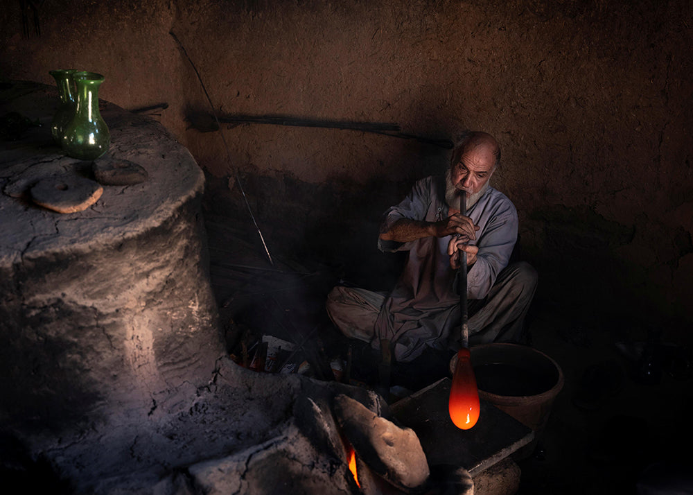 Man working with molten glass in a dark workshop