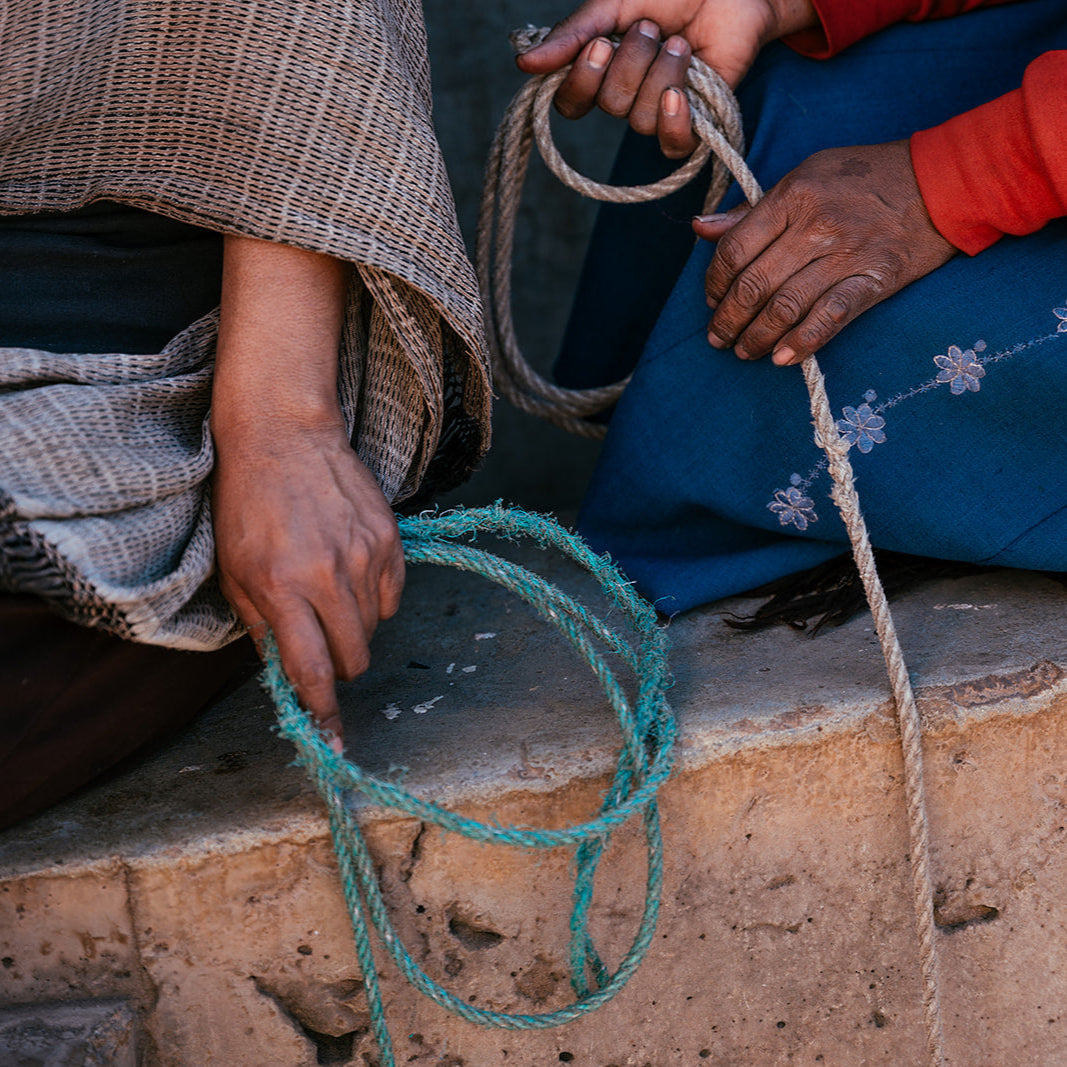 Two people sitting on a stone ledge, one holding a rope and the other a blue fabric.
