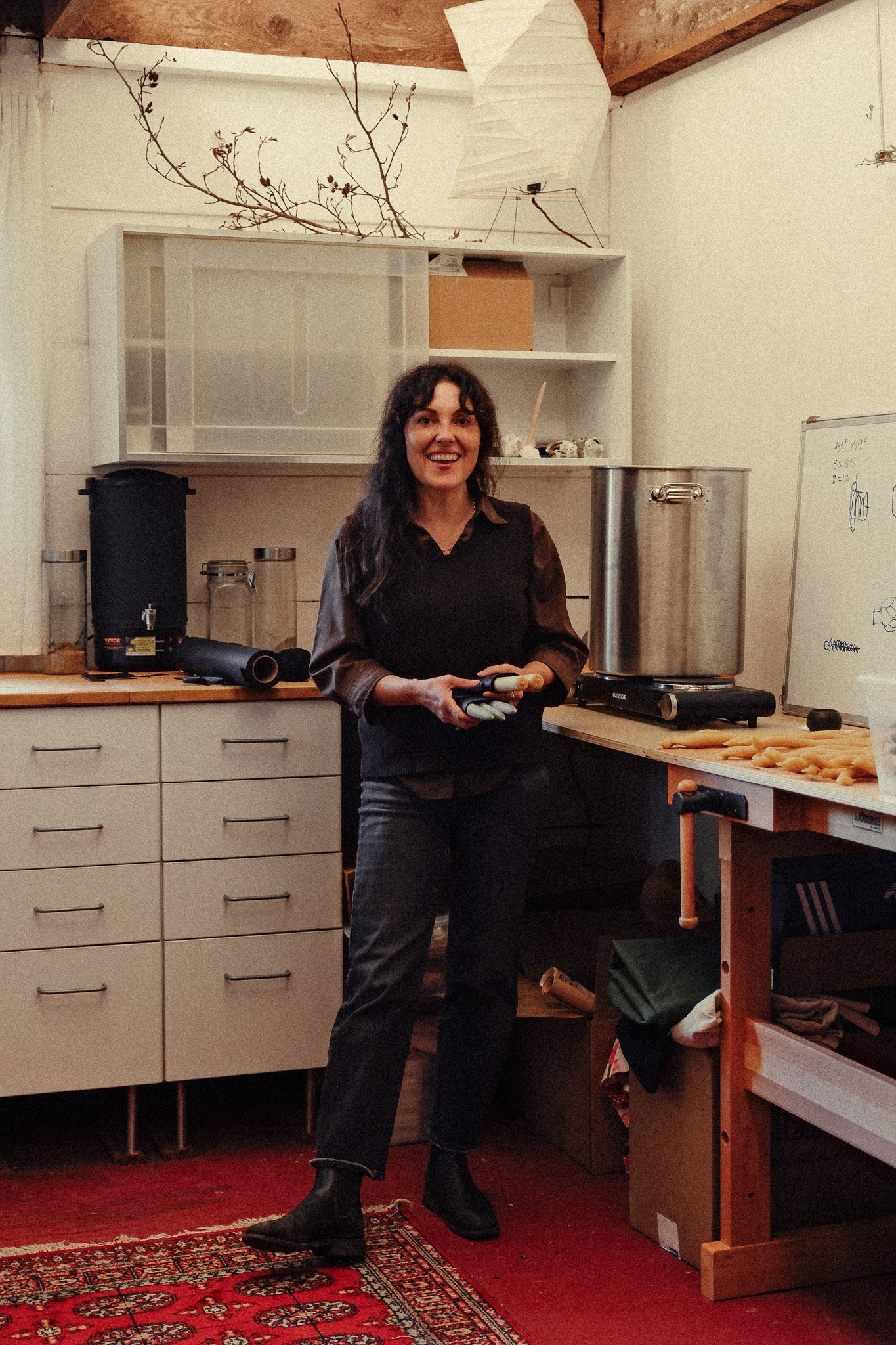 Tanya, Obakki artisan partner, with long dark hair stands in a her studio holding her handmade candles.