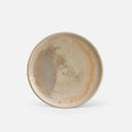 A handmade ceramic plate with a rustic, glaze featuring a mix of beige, light brown, and subtle orange-brown variations, shown on a clean white background.