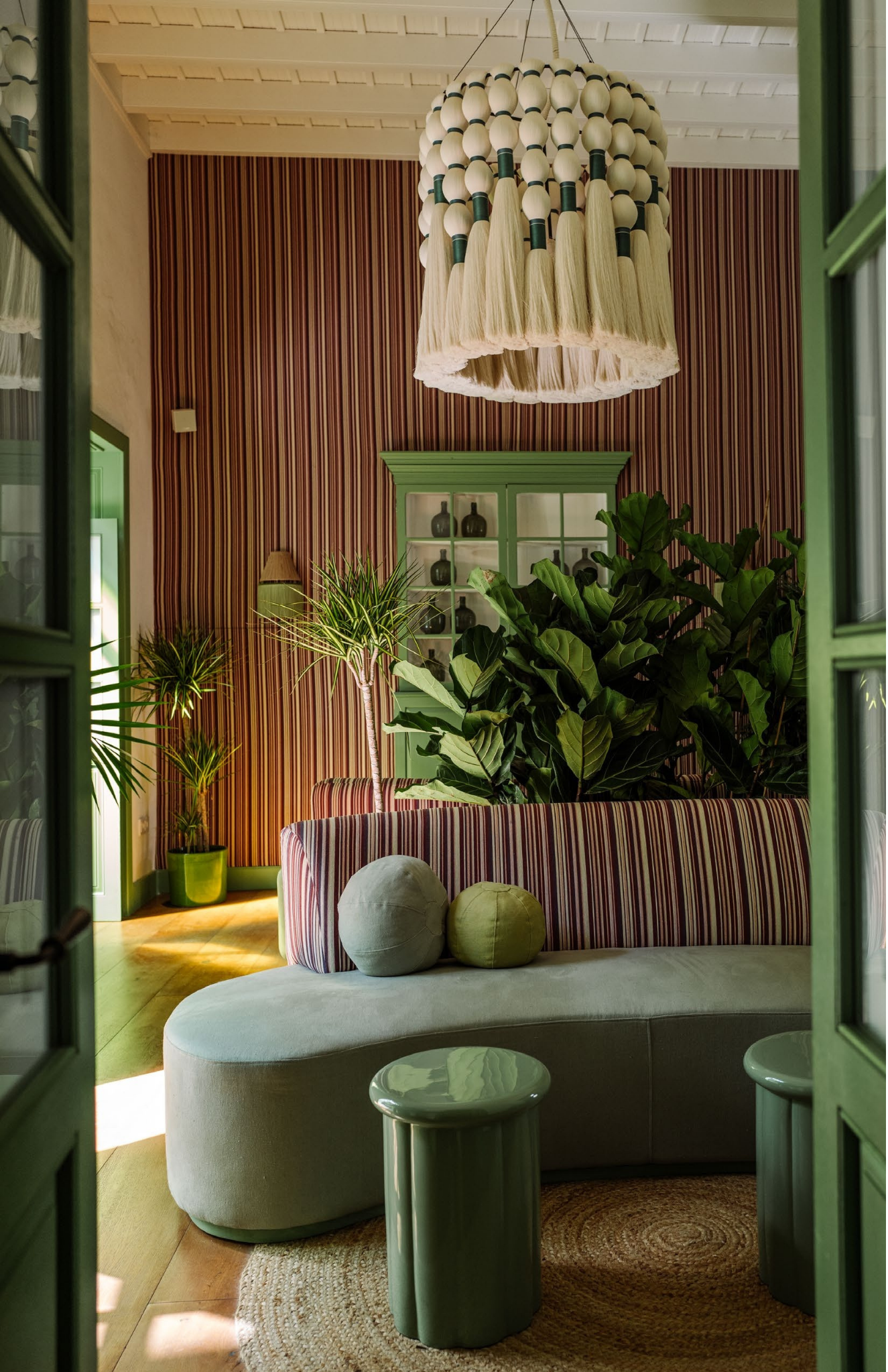 Hotel lounge interior with a Caralarga chandelier, striped sofa, and indoor plants, showcasing artisan pieces available through Obakki.