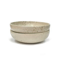 Two beige speckled ceramic bowls stacked on a white background