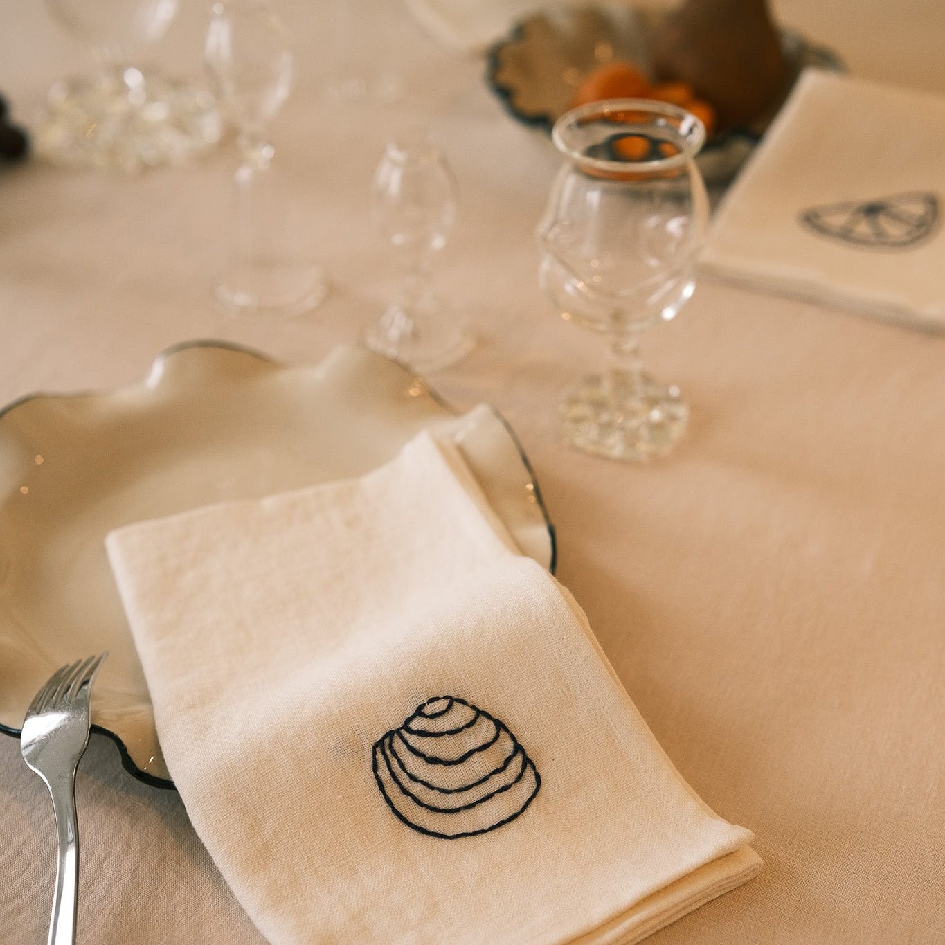 Linen napkin with shell design on a table setting with cutlery and glasses.