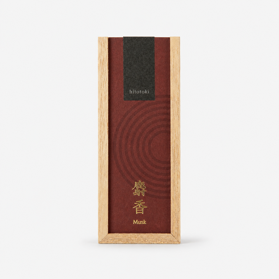 A rectangular incense box with a light natural wood frame and a dark reddish-brown lid featuring concentric circular texture, a black 'hitotoki' label near the top, and gold Japanese characters with the word 'Musk' below.