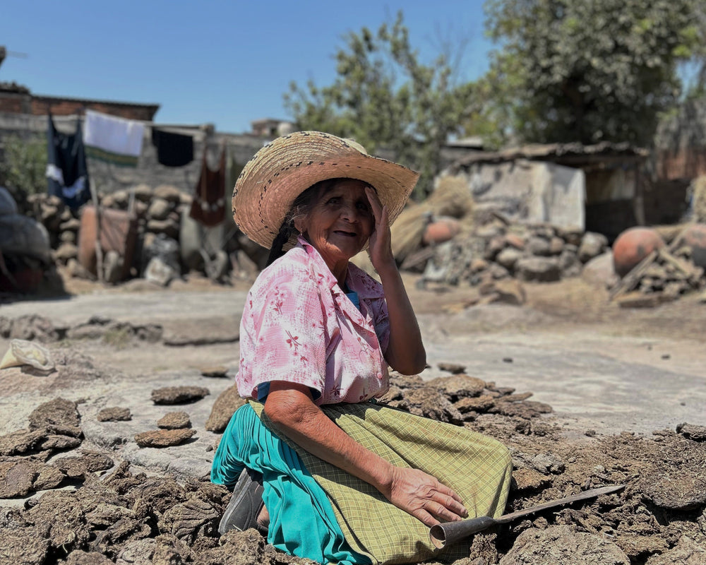 Woman sitting on a rocky surface outdoors with a straw hat and traditional clothing.