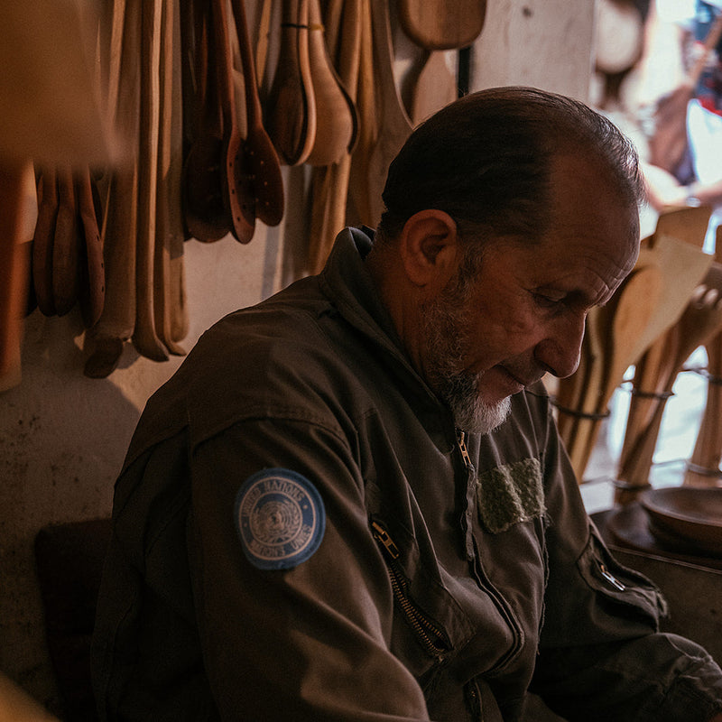 Man sitting in a rustic setting with wooden utensils hanging in the background