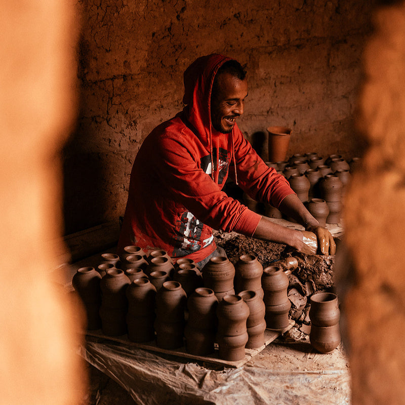 Man in a red hoodie working with clay pots in a traditional setting