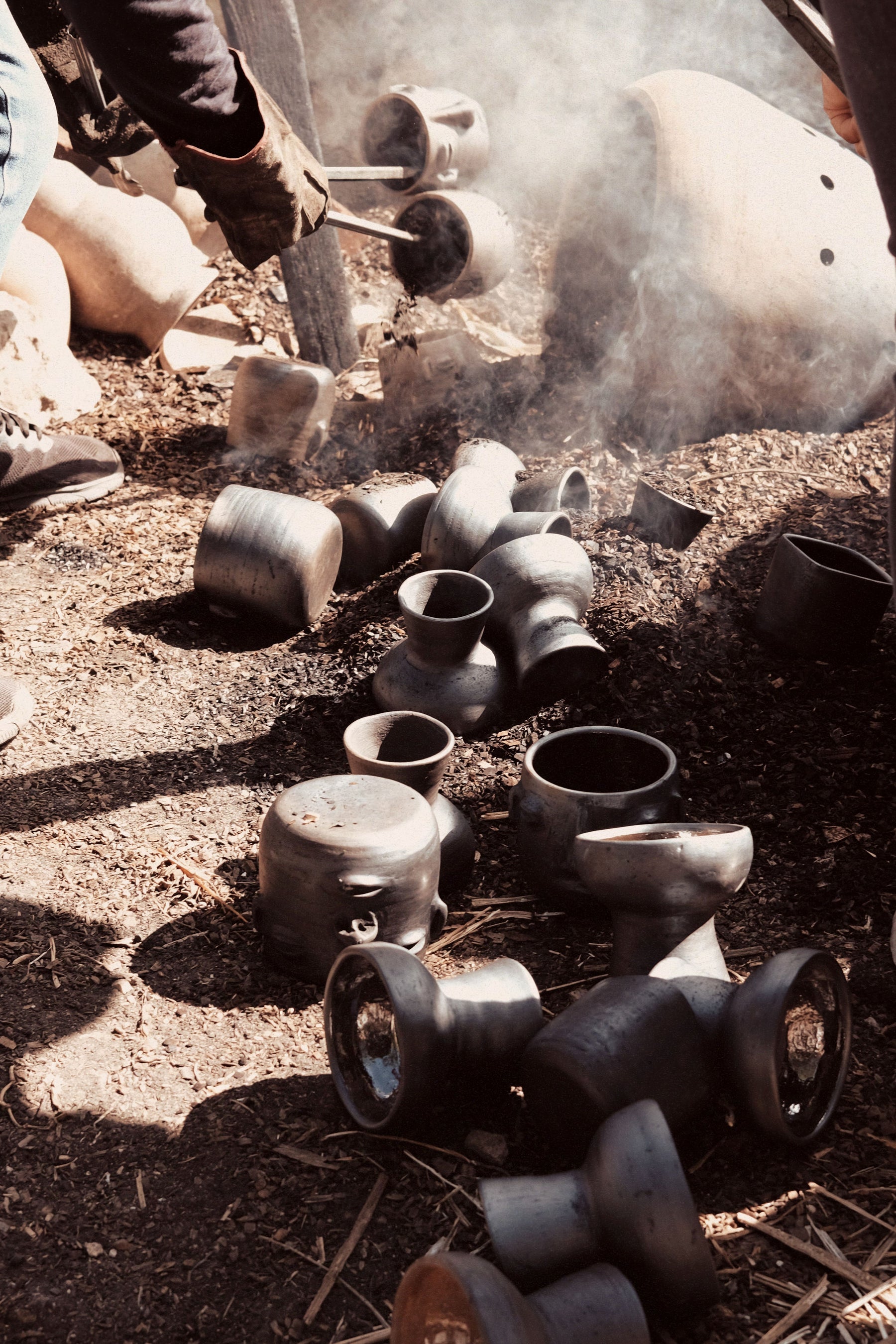 Blacksmithing process with molten metal pots on a smoky workshop floor.