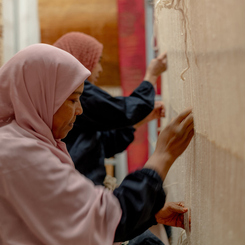 Two women wearing headscarves interacting with a stone wall.