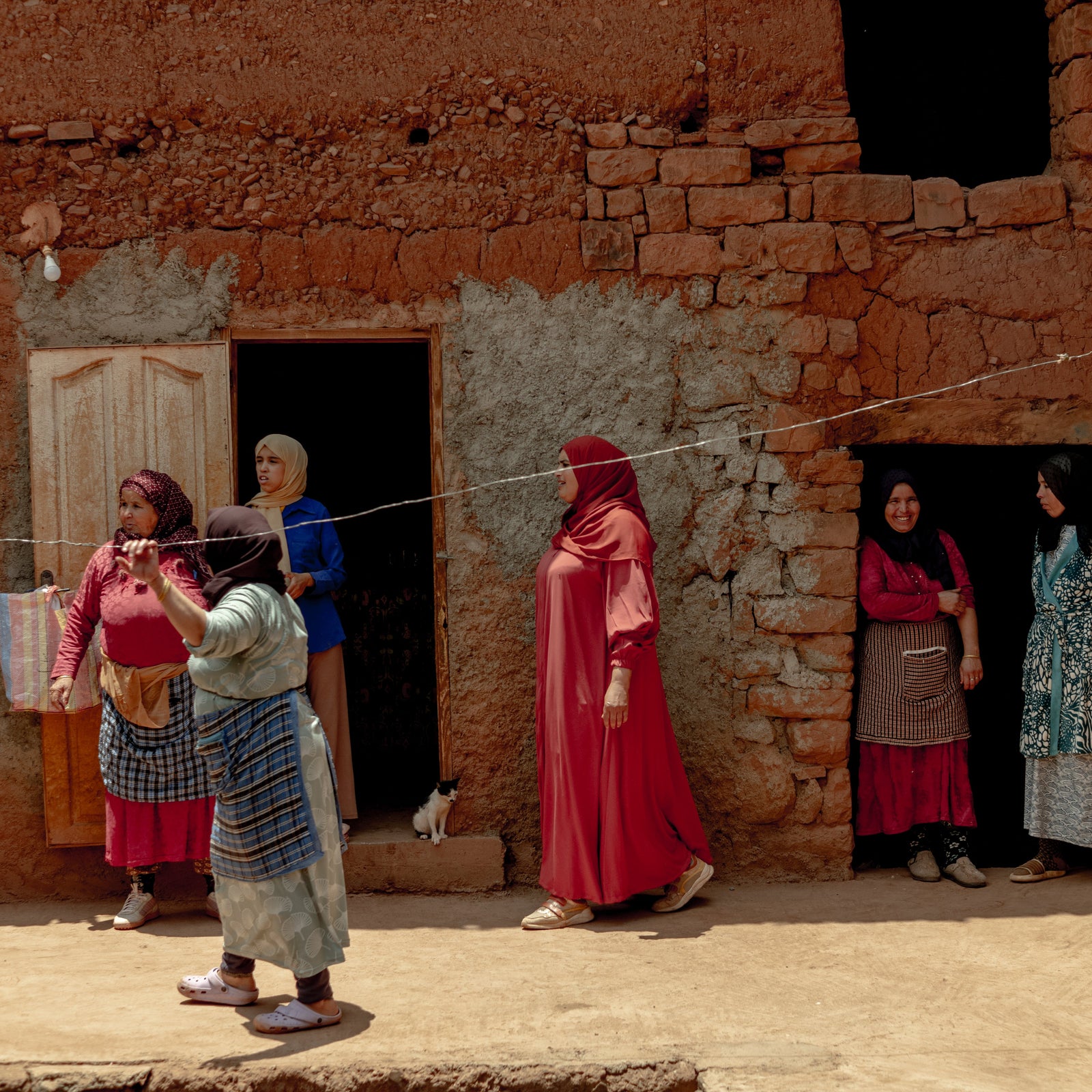 Group of women in traditional clothing standing in front of a rustic building.