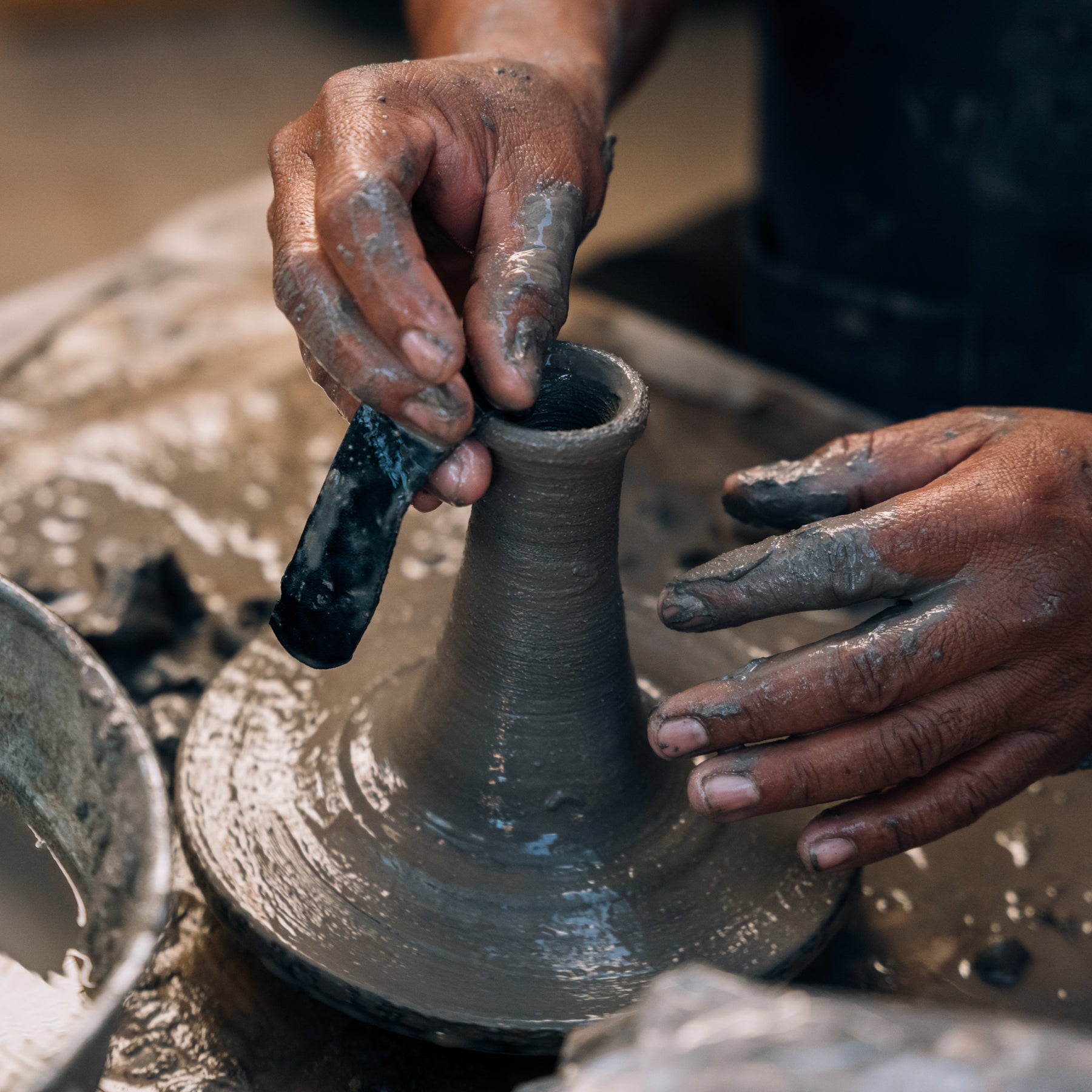 Rufina shaping a clay pot on a pottery wheel with hands covered in clay.