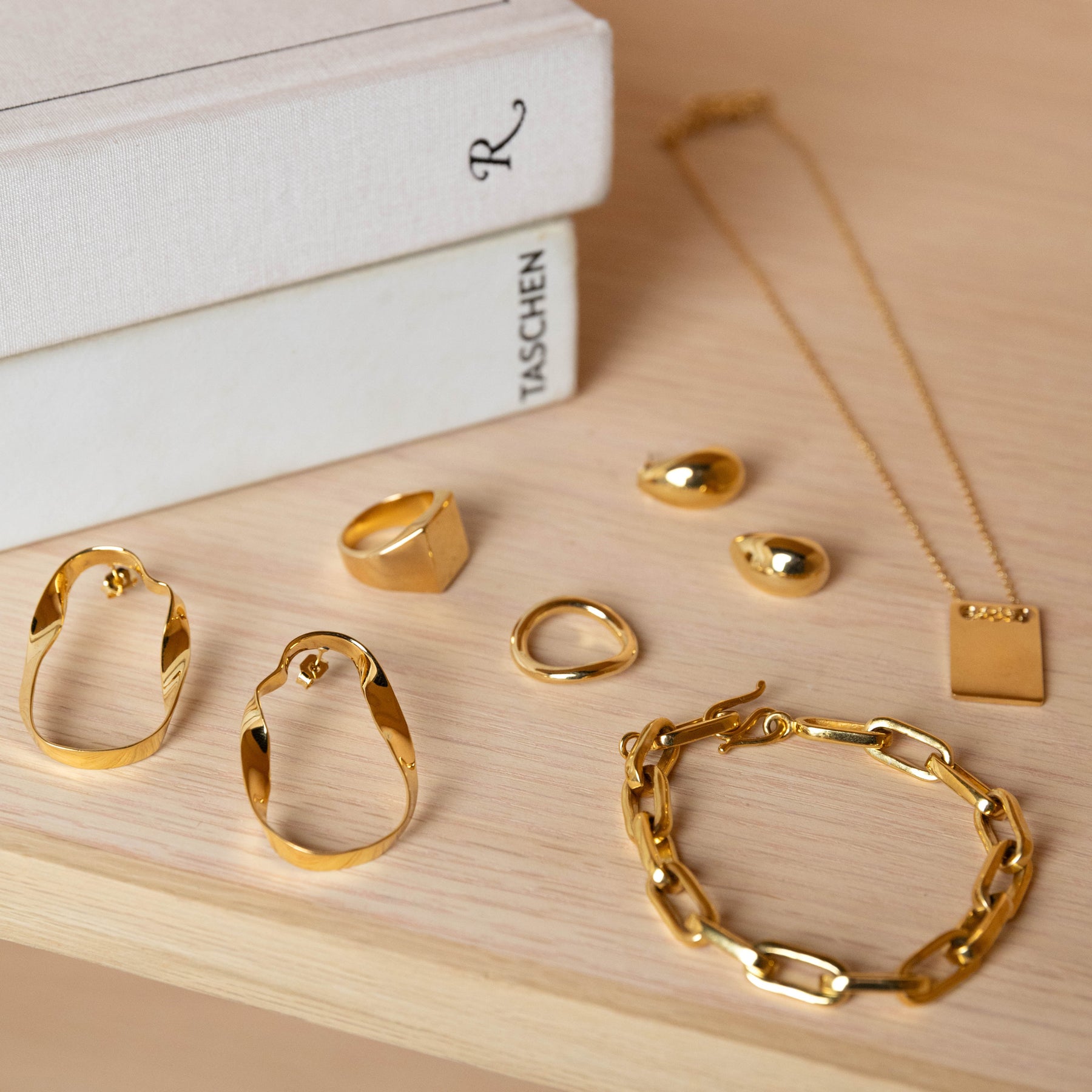 Gold plated earrings, rings, necklaces, and bracelets sit together next to a pair of books on a table.
