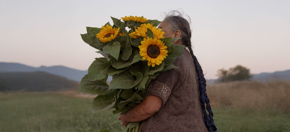 A woman holds a bundle of sunflowers in a field.