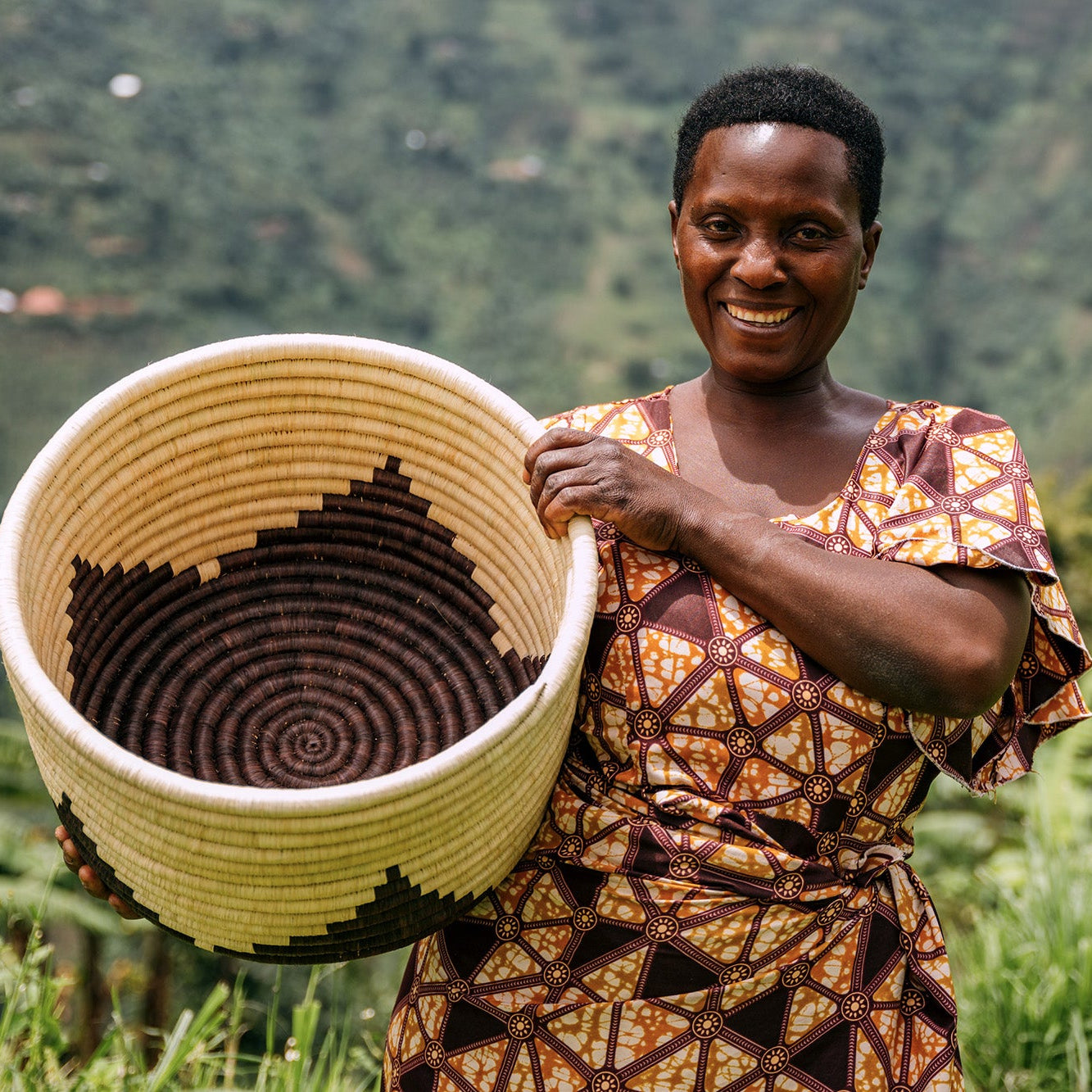 A weaver from Kasese holding her basket up and smiling.