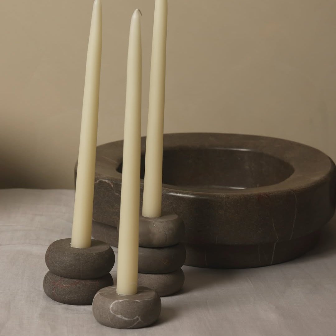 Three tall, white candles in stone candle holders on a neutral background