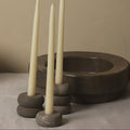 Three tall, white candles in stone candle holders on a neutral background