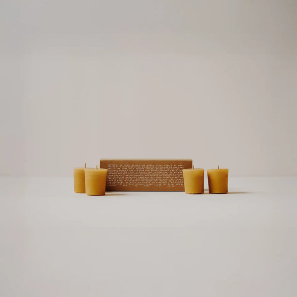 A set of natural beeswax candles arranged around a rectangular brown wooden box with engraved text, photographed on a clean white surface against a light gray background.