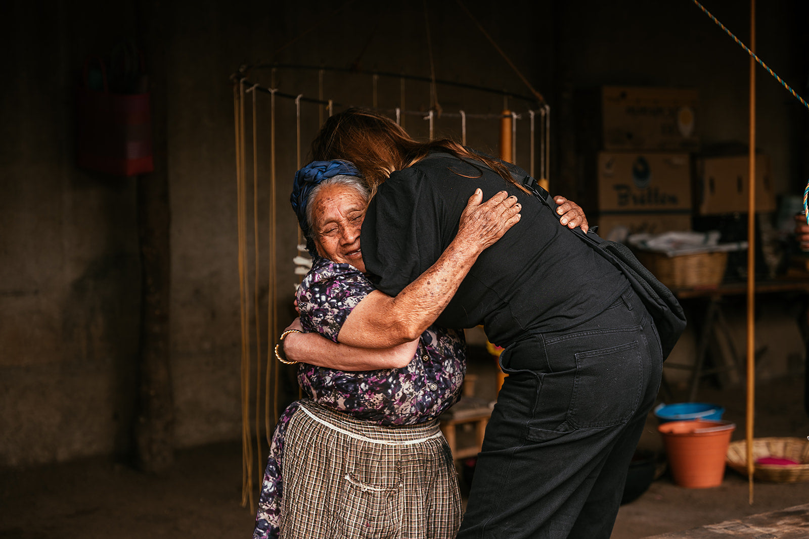 Two elderly women embracing each other in a dimly lit room.