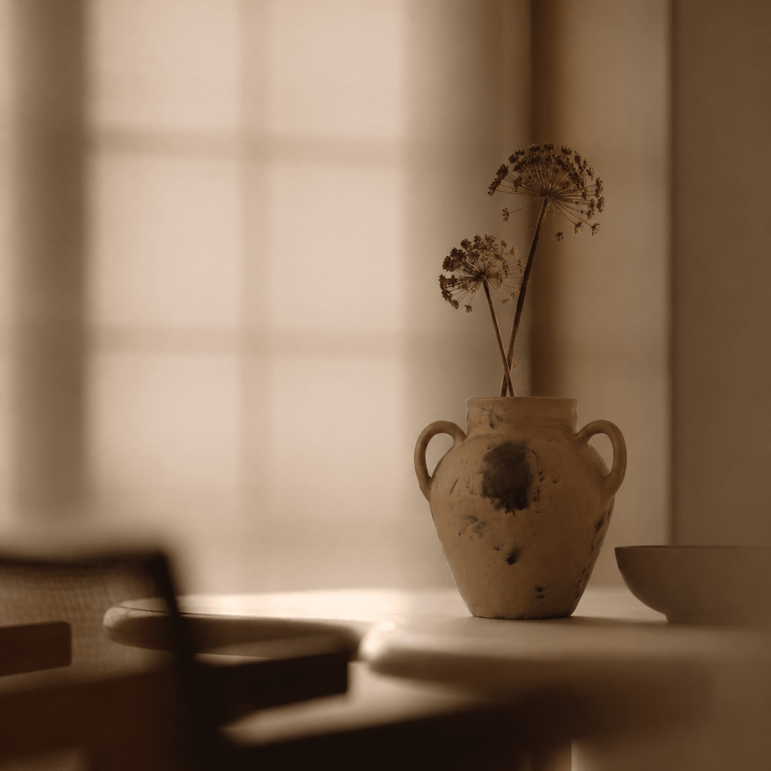 Vintage-style vase with dried flowers on a table in a softly lit room