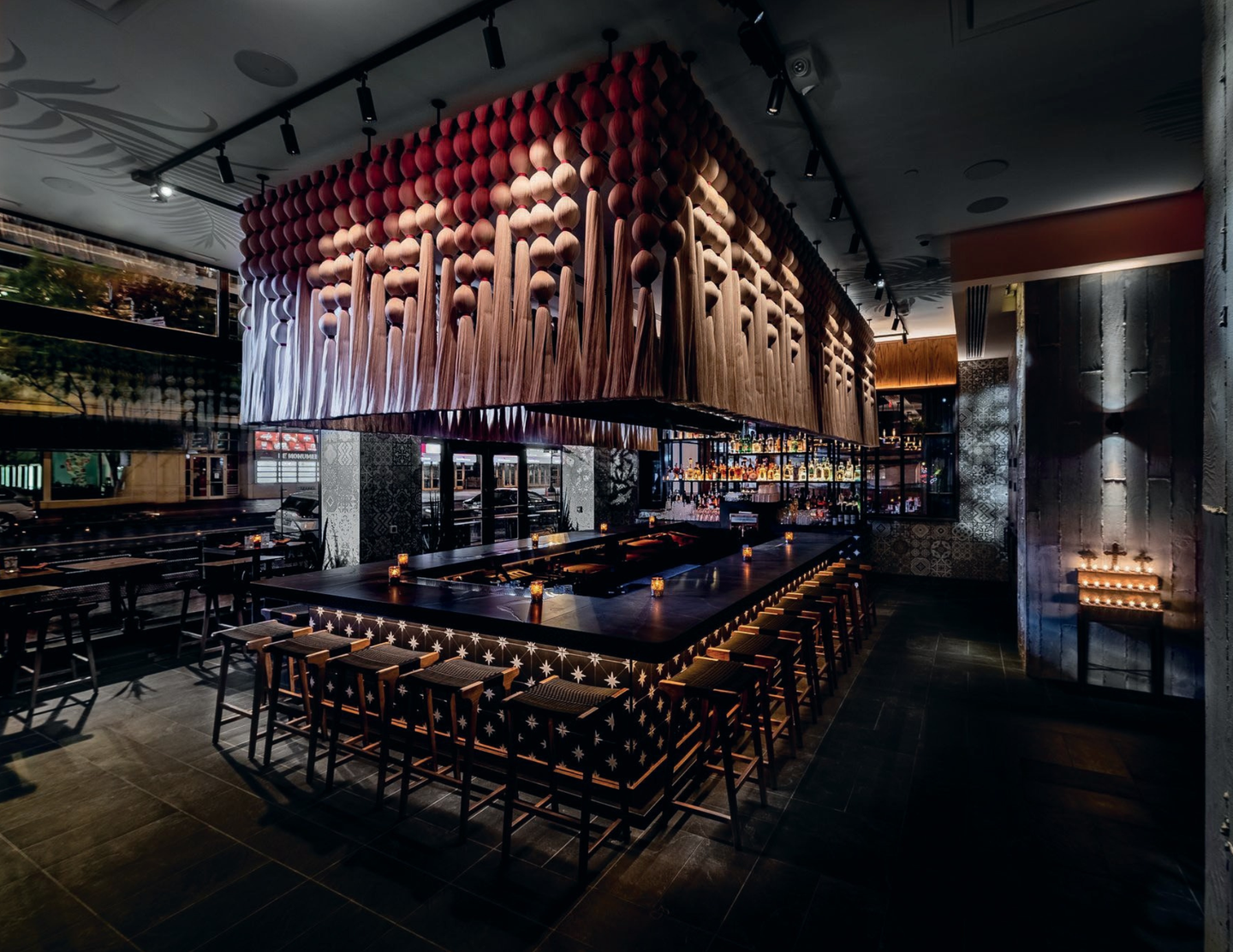 Caralarga textile installation suspended over a central bar in a restaurant interior, featuring wood stools and candlelit seating.
