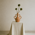 Ceramic vase with flowers on a white cloth-covered table against a beige wall.