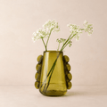 Green vase with decorative elements holding flowers on a beige background
