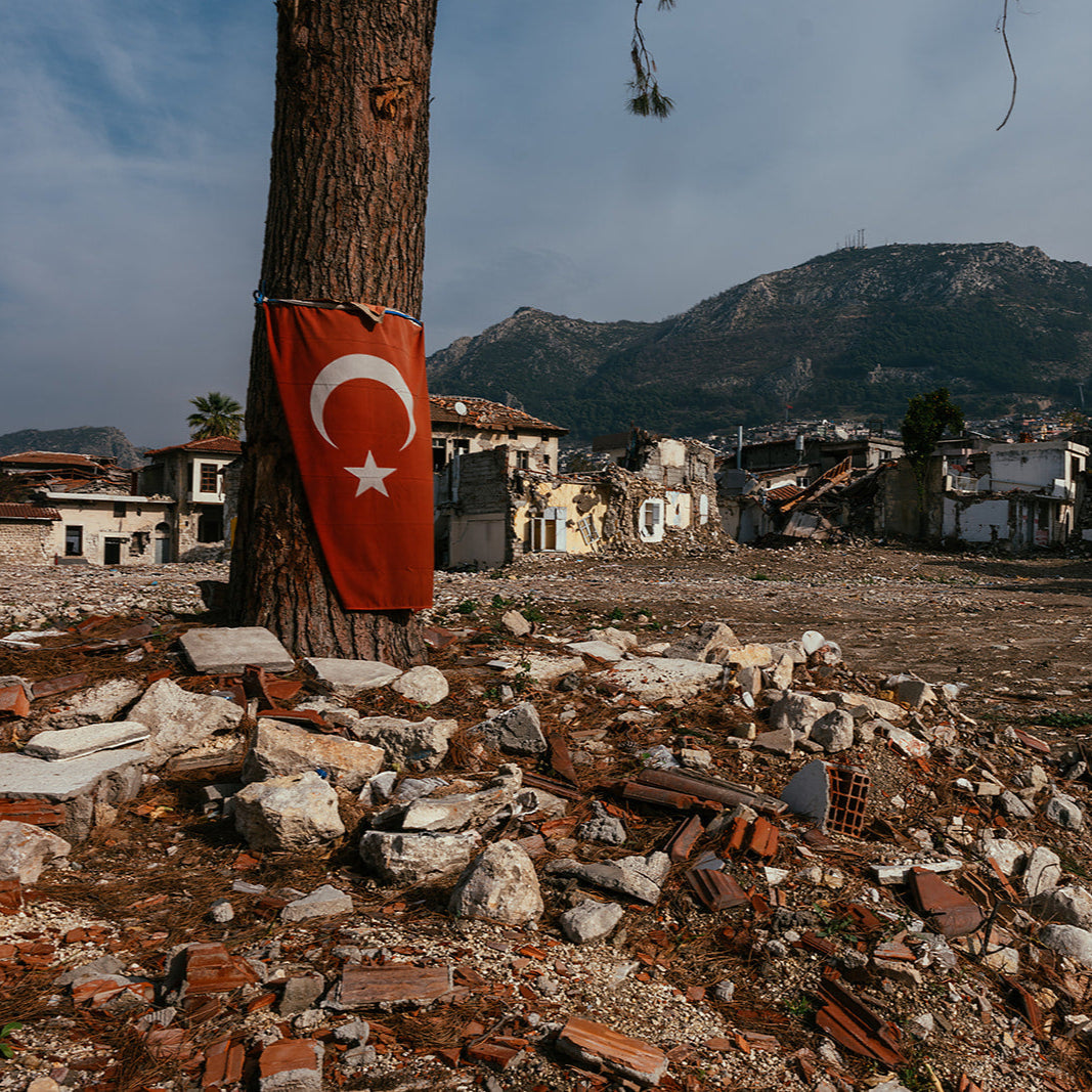 Ruins with a Turkish flag attached to a tree, surrounded by mountains and rubble.