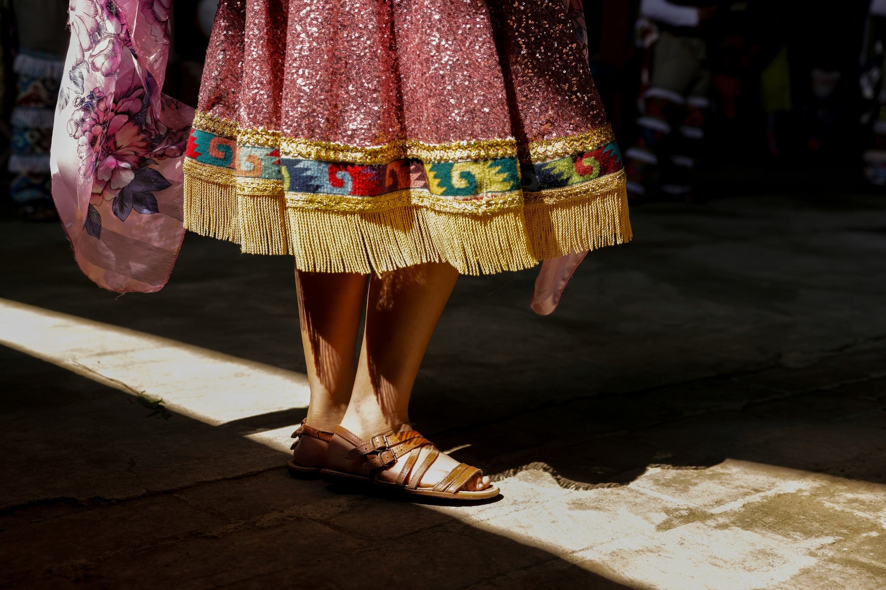 Person wearing a colorful skirt with fringe and sandals on a dark floor - oaxaca culture
