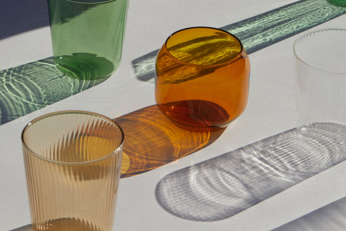 Three glass tumblers on a textured surface with green, orange, and clear colors.