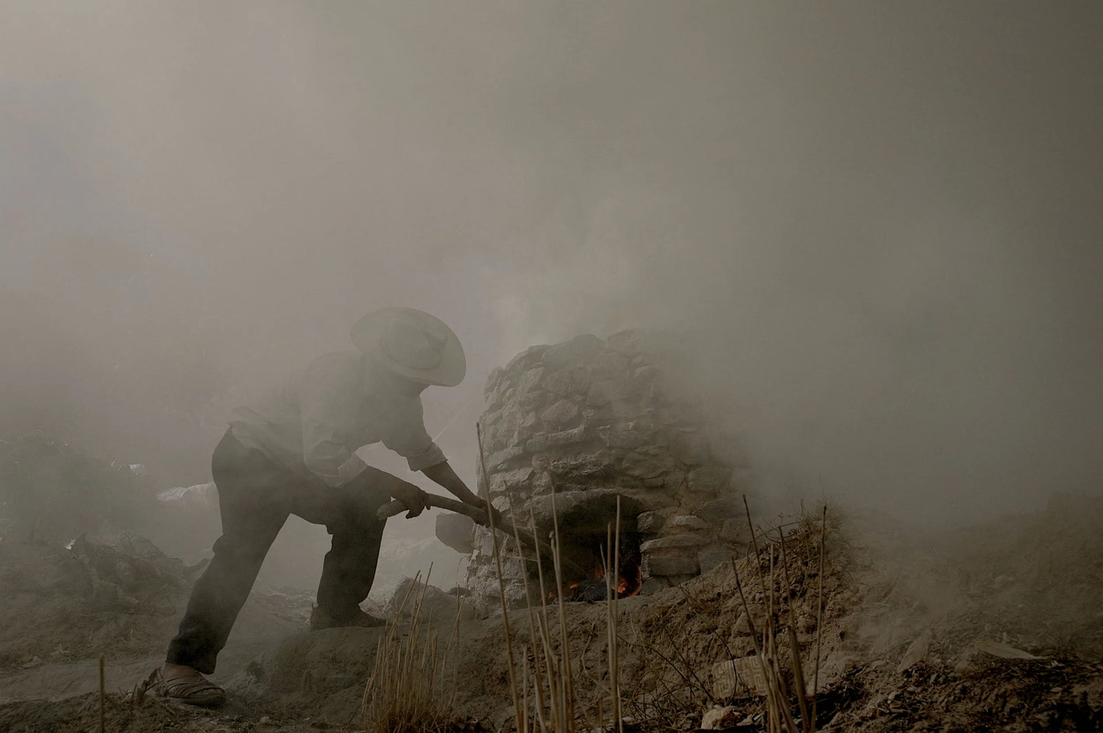 Person in military gear crouching behind a rock in a foggy, war-torn landscape, black clay oaxaca