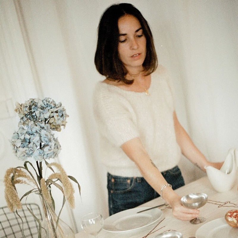 Woman setting a table with silverware and a vase of flowers.